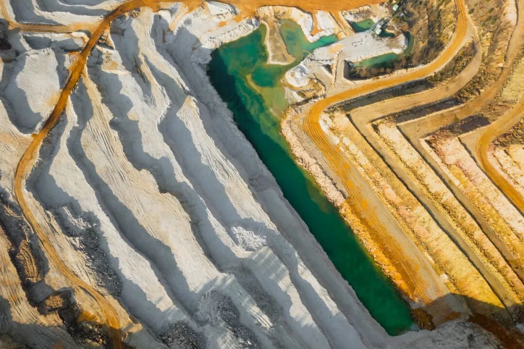 Top view on a sand quarry. Arial view on a mining of natural resources or ore. Green river separates white and yellow sand shores..jpg